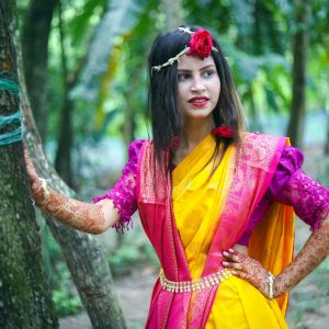 A young South Asian woman poses gracefully in a colorful saree outdoors, showcasing traditional elegance.