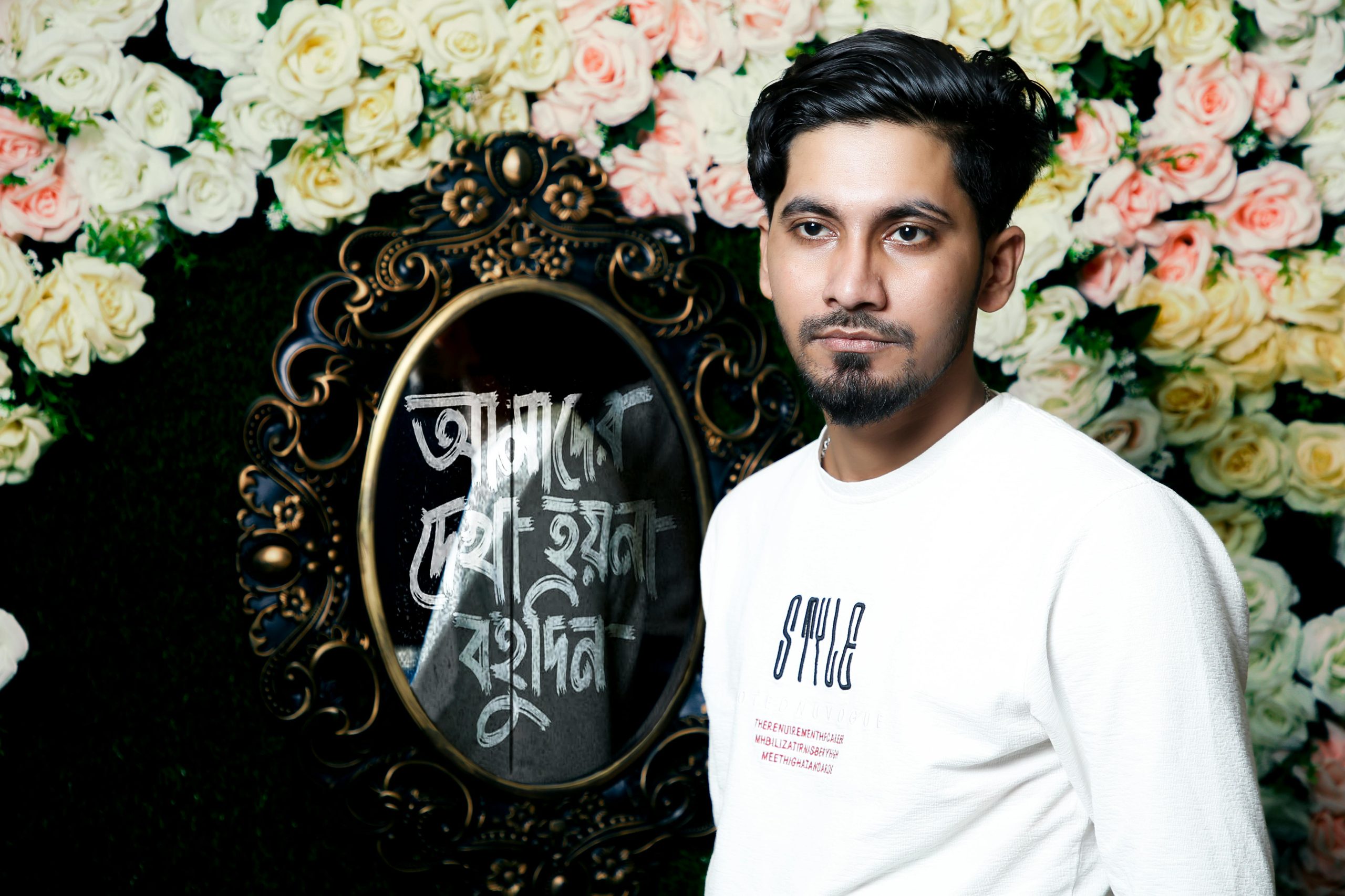 Portrait of a young man in front of an ornate mirror surrounded by flowers, creating an elegant and artistic atmosphere.